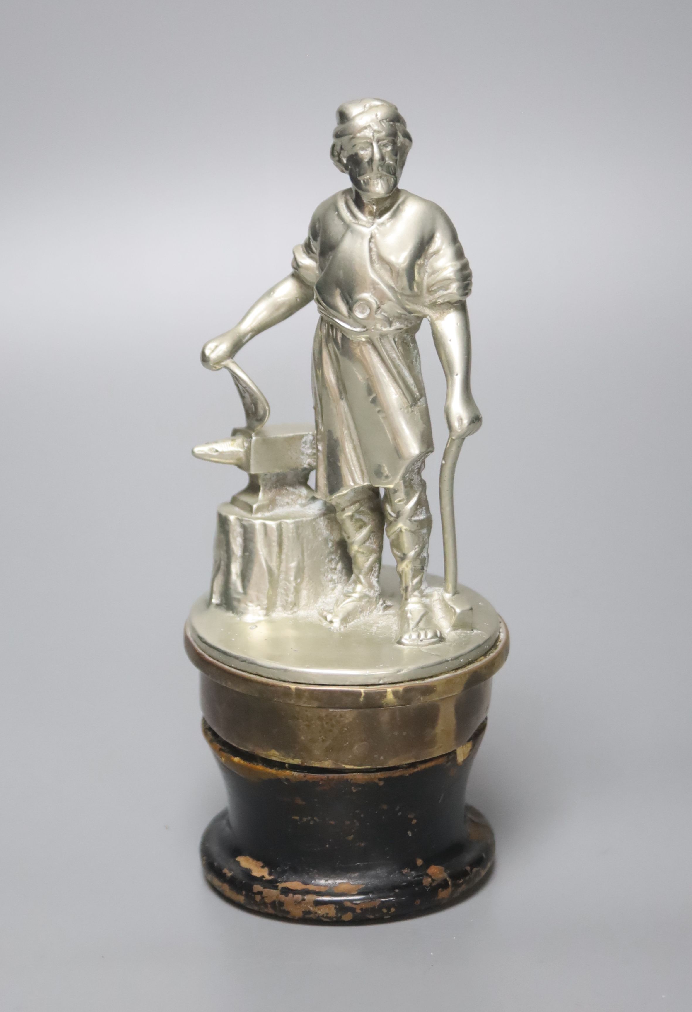 A large cast metal Vulcan car mascot, in the form of a blacksmith, on brass base and lacquered wooden socle, 18cm high